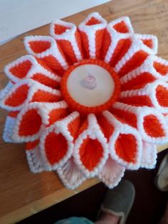 an orange and white crocheted flower sitting on top of a wooden table next to someone's feet