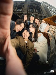 a group of young people taking a selfie in front of a tall building with their arms around each other