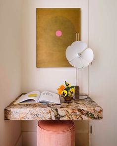 a table with a lamp, book and vase on it in front of a painting