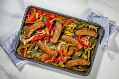 sausages, peppers and onions in a pan on a white counter top with napkins