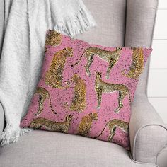 a pink and gold leopard print pillow on a grey chair next to a throw blanket