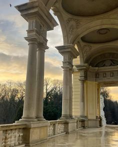 an ornate building with columns and arches on the outside, in front of trees at sunset