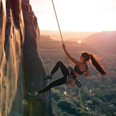 a woman climbing up the side of a cliff with her hands in the air while holding onto a rope