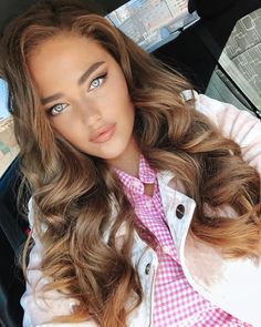 a woman with long brown hair and blue eyes sitting in a car looking at the camera