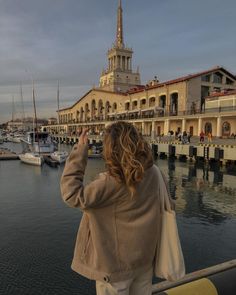 a woman taking a photo of boats in the water near a building with a steeple on top