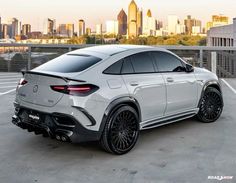 the rear end of a white mercedes suv parked in a parking lot with cityscape in the background