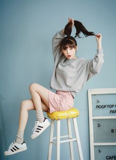 a young woman sitting on top of a stool with her hair in the air and wearing adidas shoes