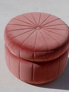 a pink round ottoman sitting on top of a cement floor next to a white wall