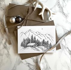 a card with a drawing of a cabin in the woods on it next to two ornaments