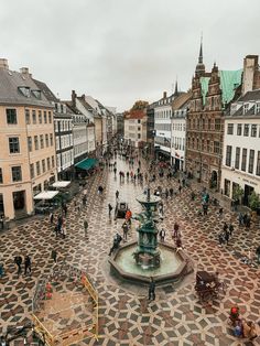 an aerial view of people walking around in a city square with a fountain and clock tower