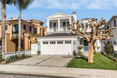 a white house with palm trees in the front yard and two story houses behind it