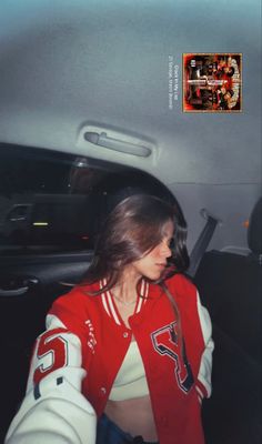 a woman sitting in the back seat of a car wearing a red and white jacket