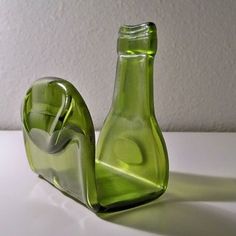 a green glass bottle sitting on top of a white table next to a vase filled with water