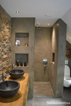 two black bowls are on the counter in this modern bathroom with stone walls and flooring