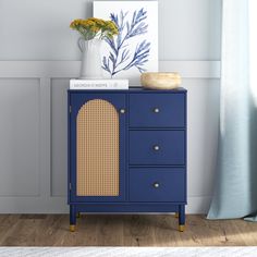 a blue cabinet with wicker doors and gold handles in a room next to a window