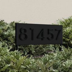 a black house number sign in front of bushes