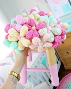 a person holding up a bunch of colorful crocheted balls on top of a stool