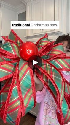 a woman holding a giant christmas bow with a red ball on it's head