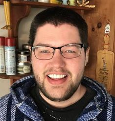 a man with glasses is smiling at the camera in front of some shelves and jars