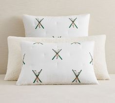 two white pillows with green and red crossed skis on them sitting next to each other