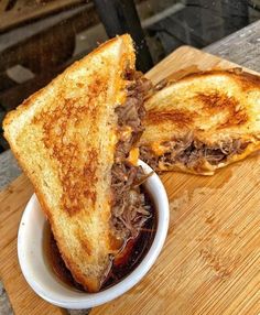 a sandwich cut in half sitting on top of a wooden cutting board next to a bowl of chili