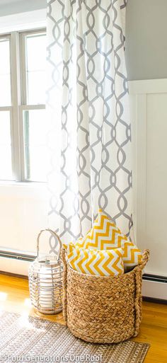 a basket with yellow and white pillows sitting in front of a window next to a rug