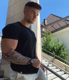 a man with a tattoo on his arm standing next to stairs and looking at the camera