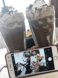 a cell phone sitting on top of a wooden table next to two glasses filled with liquid