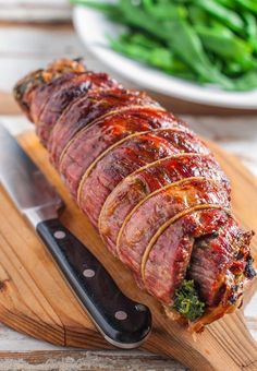 a large piece of meat on a cutting board with a knife and some green vegetables