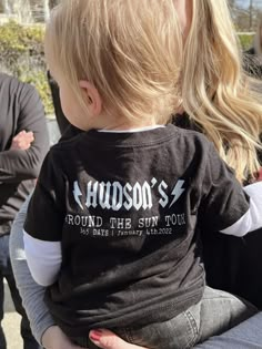 a woman holding a small child in her lap and wearing a shirt that says hudson's round the sun tour