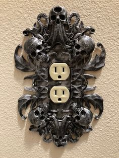 an intricately designed outlet cover with skulls and bones on it's side is mounted to the wall