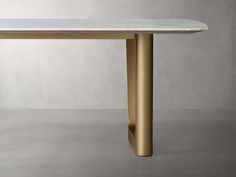 a white marble table with gold legs on a grey floor in front of a gray wall