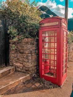 a red phone booth sitting next to a stone wall