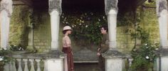 two people standing in front of an old building with vines growing on the walls and pillars