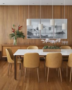 a dining room table with yellow chairs and pictures hanging on the wall above it, along with potted plants