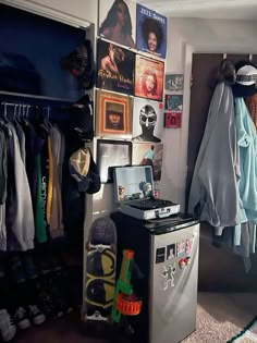 a small room with clothes hanging on the wall and a refrigerator in front of it