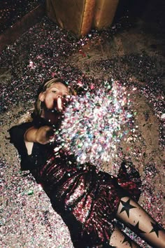 a woman laying on the ground surrounded by confetti in her hand and looking at the camera