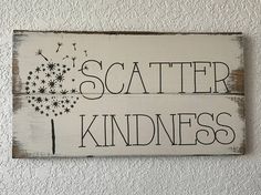 a wooden sign that says, scatter kindness and dandelion on it's side