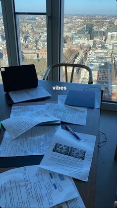 there are many papers on the table in front of the window with view of the city