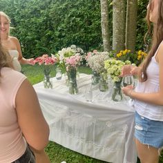 two women standing at a table with flowers in vases on it and one woman holding out her hand