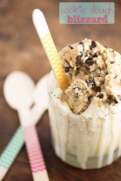 a cookie dough blizzard in a glass with a straw and spoon next to it on a wooden table