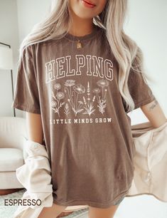 a woman with long blonde hair wearing a brown shirt that says helping little minds grow