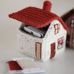 a small knitted house with a cell phone in the front and two smaller houses behind it