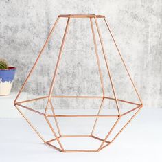 a copper geometric vase sitting on top of a white table next to a potted plant