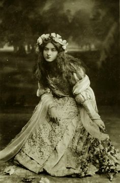 an old black and white photo of a woman wearing a dress with flowers in her hair