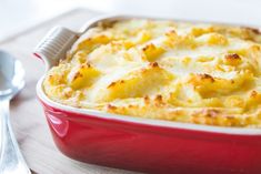 a red casserole dish filled with macaroni and cheese on a wooden table