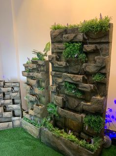 an indoor garden with rocks and plants growing out of the top, in front of a white wall