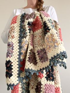 a woman is holding up a crocheted blanket