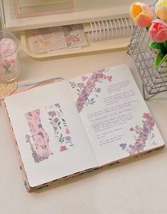 an open book sitting on top of a desk next to a vase filled with flowers