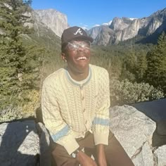 a man sitting on top of a rock next to trees